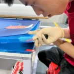 A technician applying easy-to-peel protective film stickers to blue-light blocking acrylic TV screen protectors.