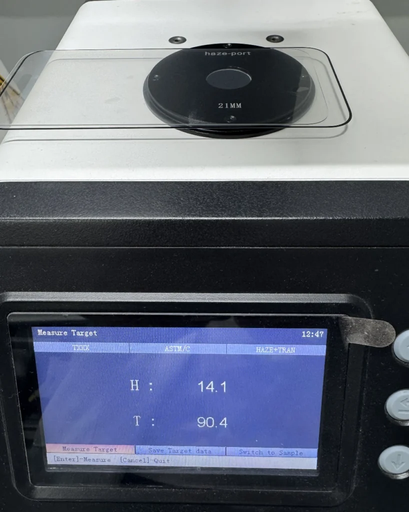 A professional haze meter testing a matte anti-glare phone screen protector, showing a haze value of 14.1 and transmittance of 90.4